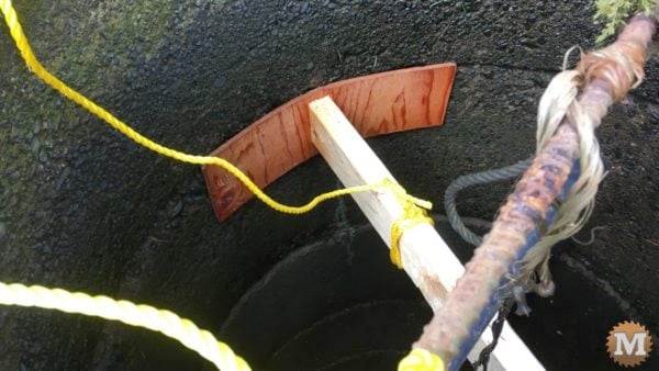 man about tools remove silt mud sediment from well Thin plywood attached to 2x4 wedged into well