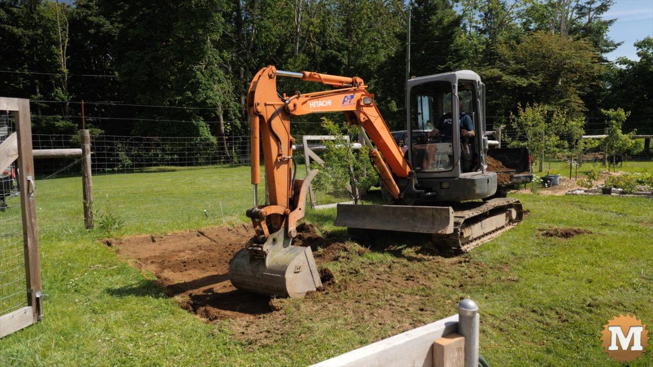 Excavator digging foundation hole for greenhouse