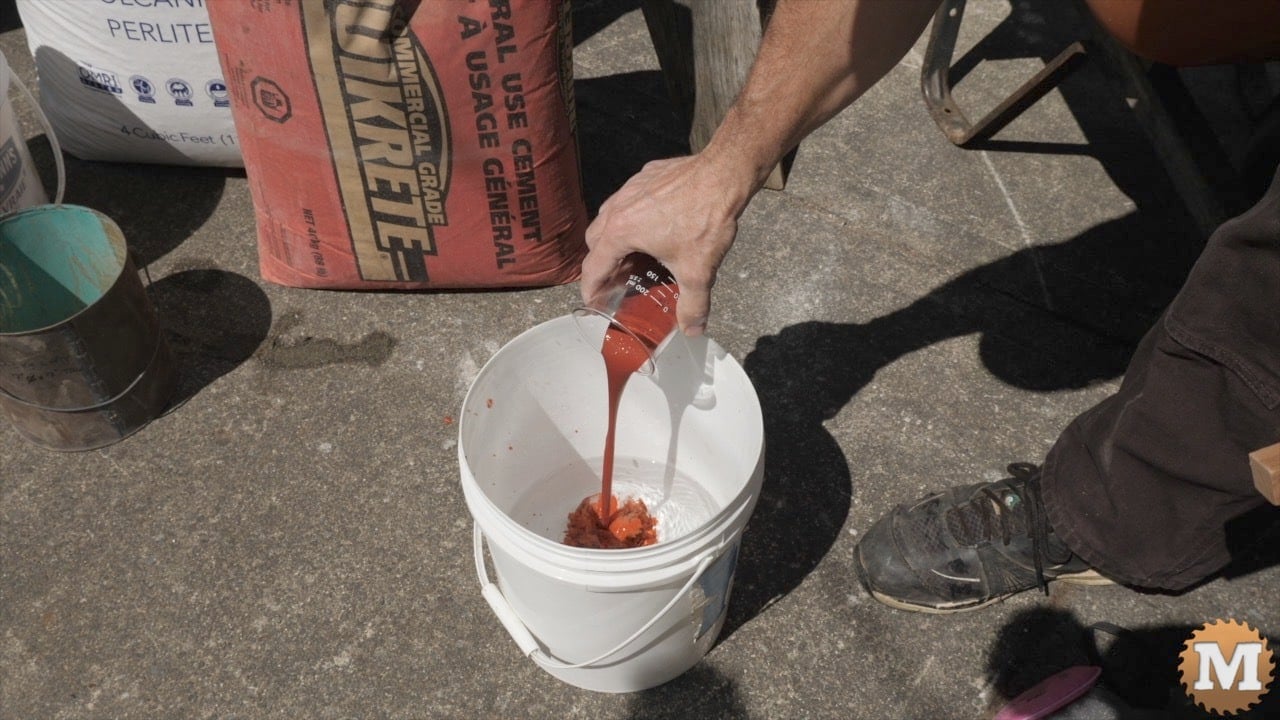 red concrete dye peing poured into a bucket with water