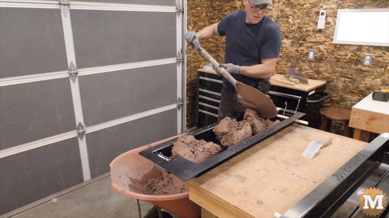 A man shvels wet concrete into a black plastic form on a table