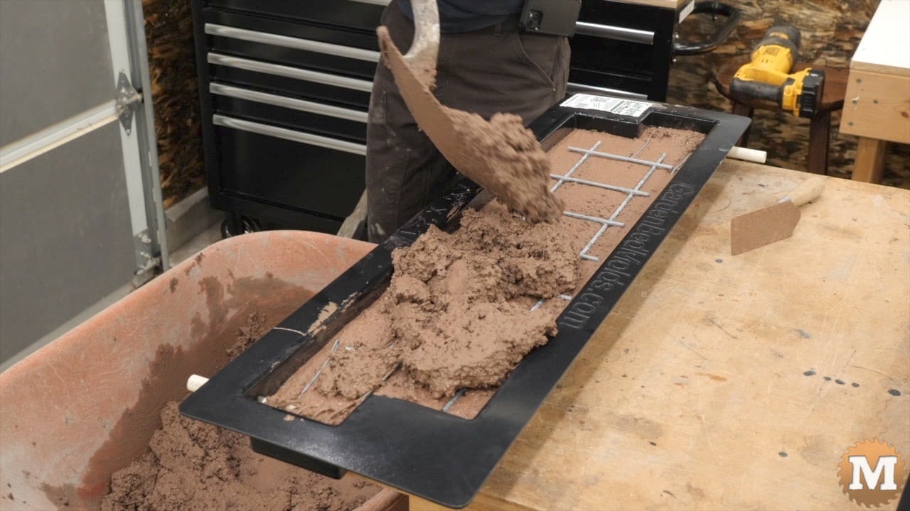 Filling a mold with red wet concrete using a shovel