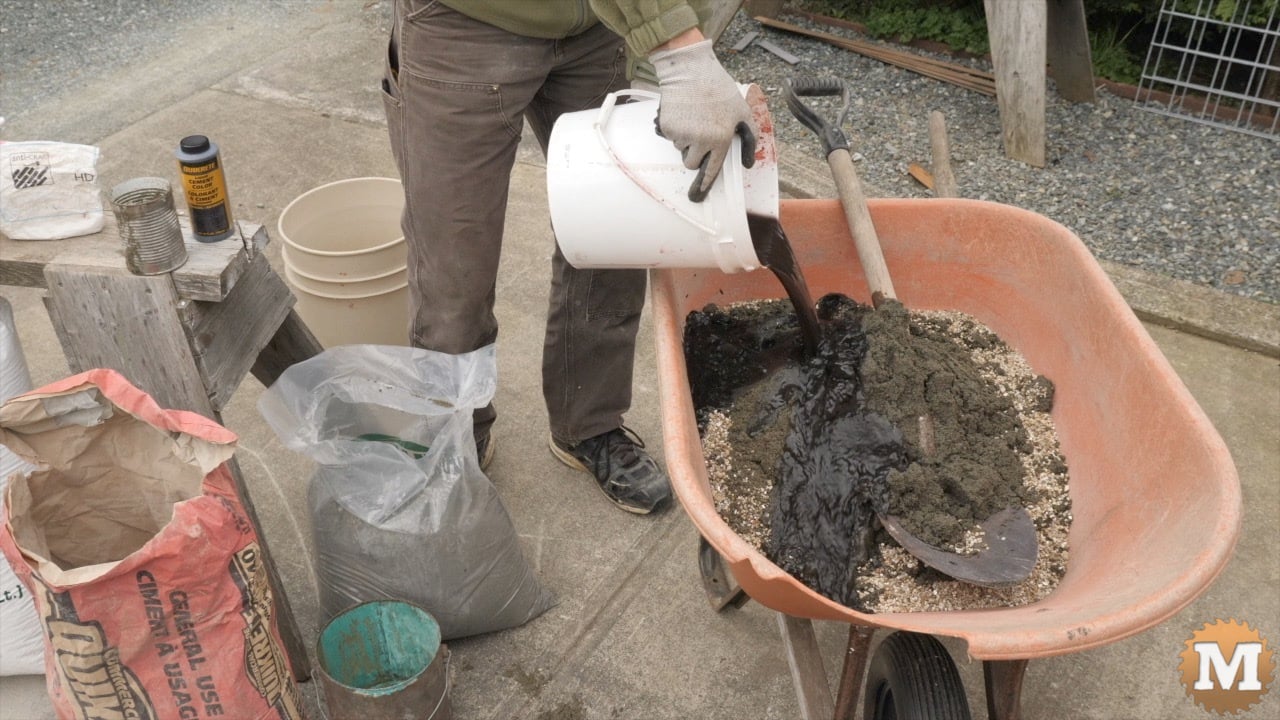 Pouring dark water from a pail onto vermiculite and sand in a wheelbarrow