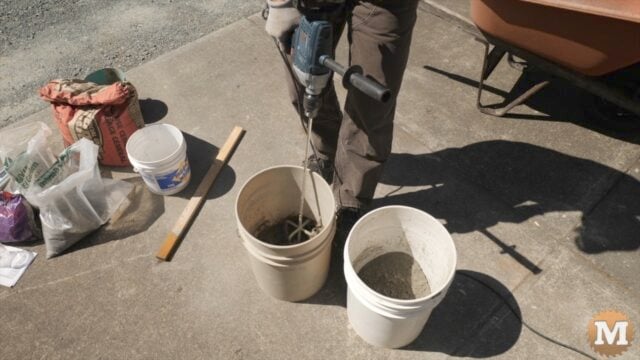 man mixing concrete in a pail using a drill