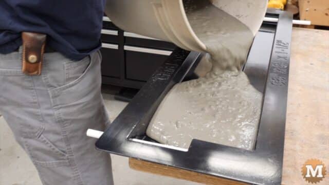 A man pours wet concrete from a pail into a plastic mold