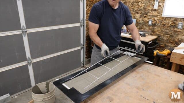 A man lays a wire grid into wet concrete in a form