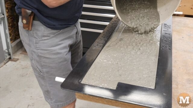 A man pours wet concrete from a pail into a plastic mold