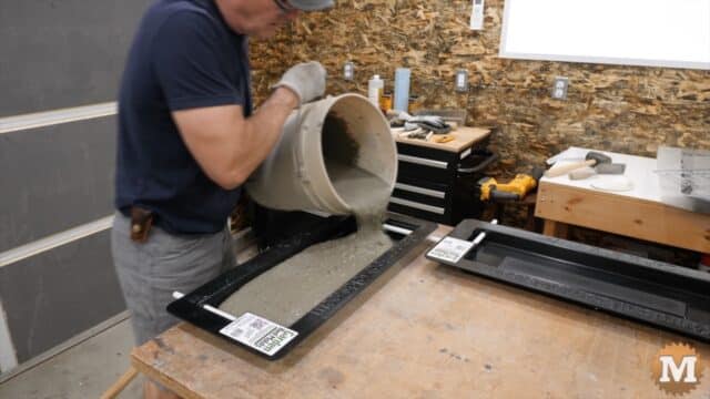 A man pours wet concrete from a pail into a plastic mold