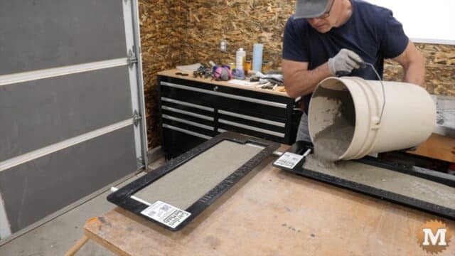 A man pours wet concrete from a pail into a plastic mold