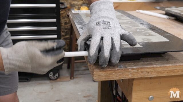 gloved hands pulling a plastic pipe from a concrete mold