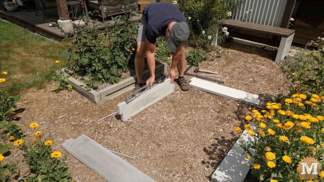 a man assembling cast concrete panels to make a raised bed in the garden