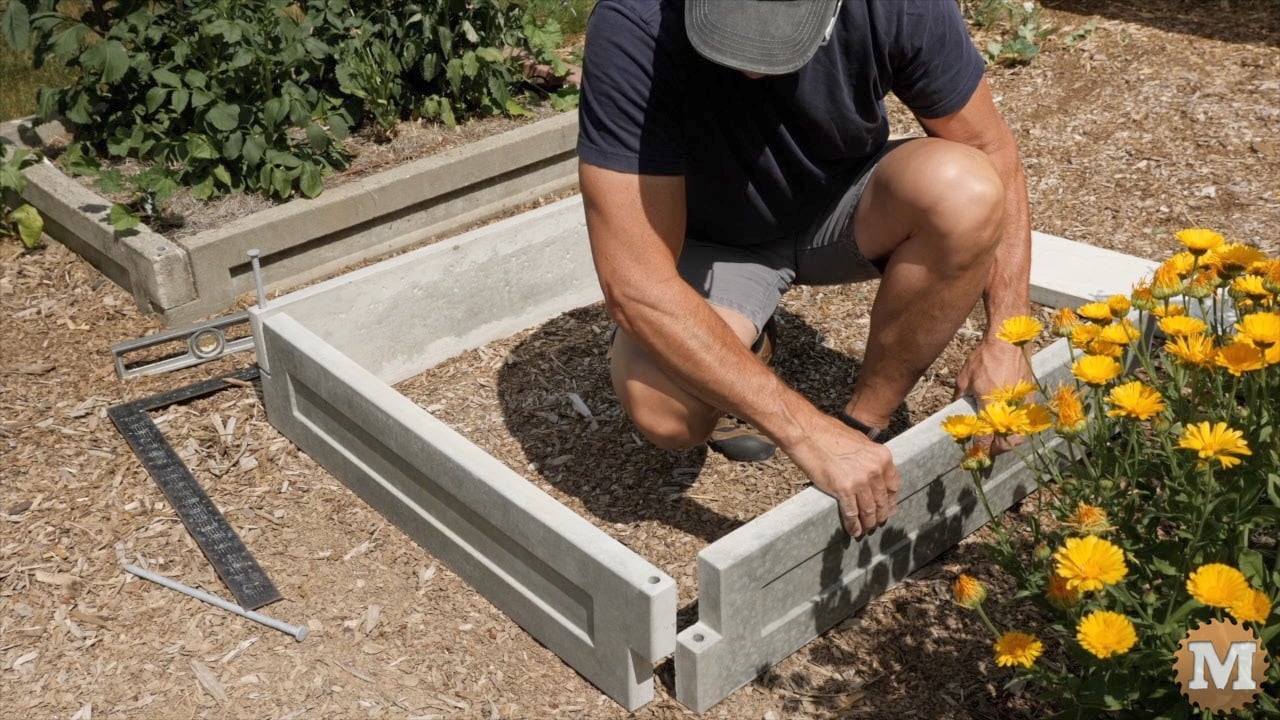 a man assembling cast concrete panels to make a raised bed in the garden