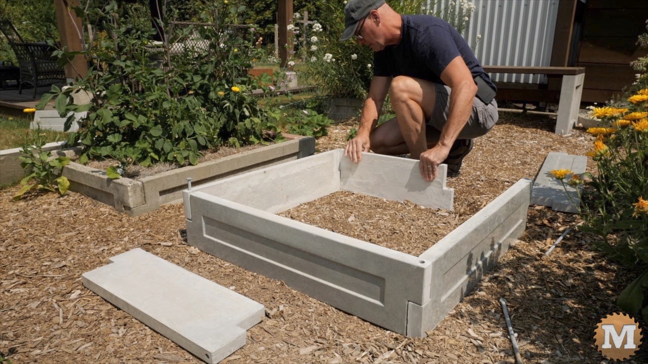 a man assembling cast concrete panels to make a raised bed in the garden