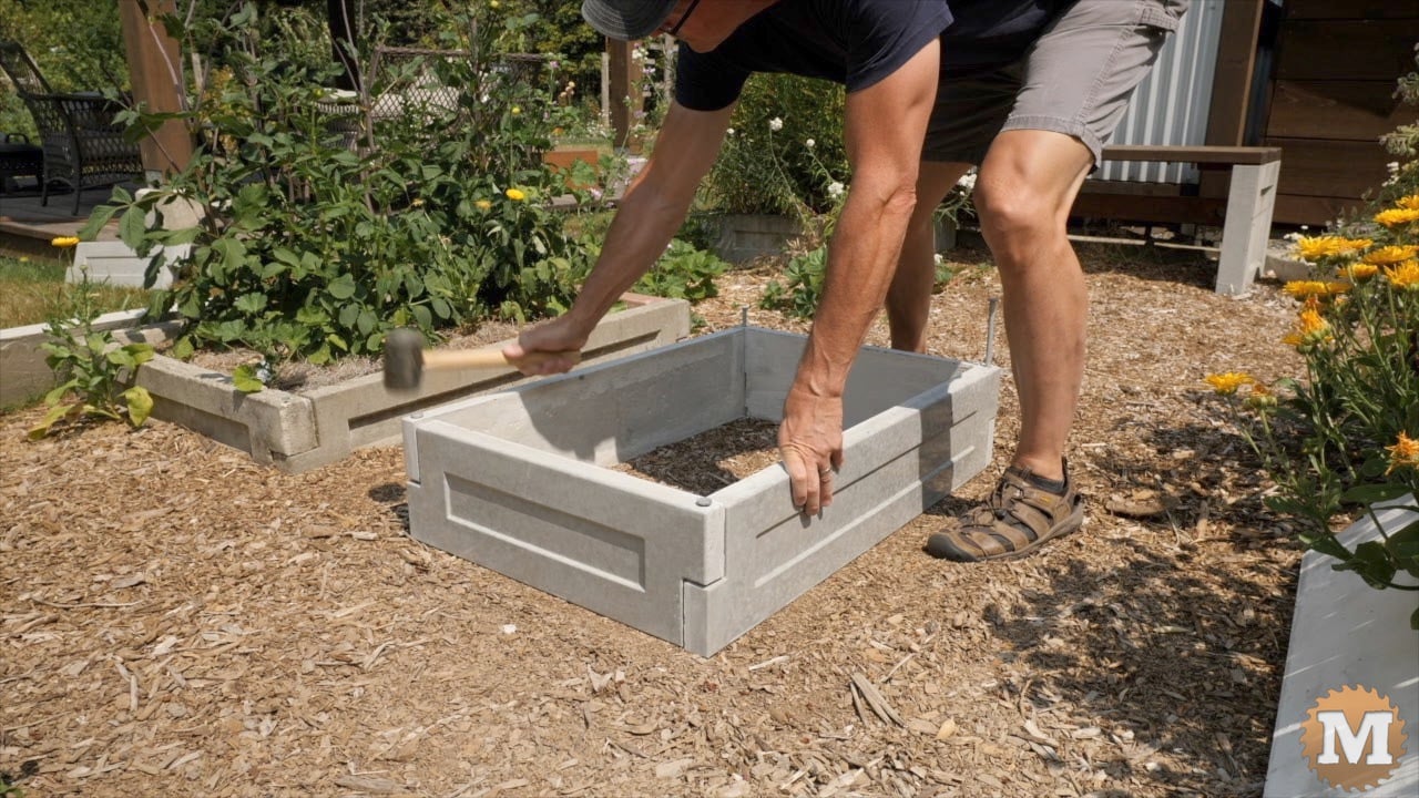 a man assembling cast concrete panels to make a raised bed in the garden