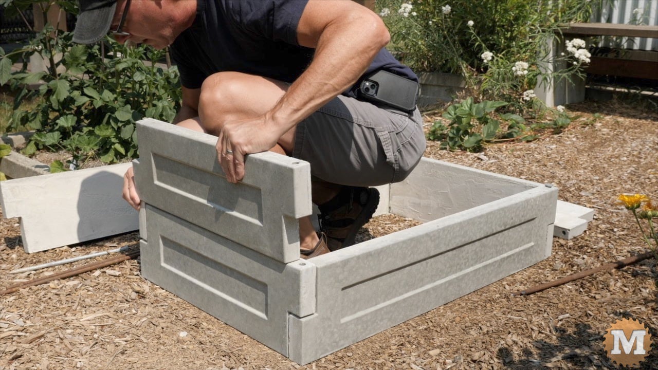 a man assembling cast concrete panels to make a raised bed in the garden