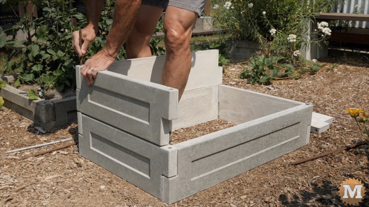 a man assembling cast concrete panels to make a raised bed in the garden
