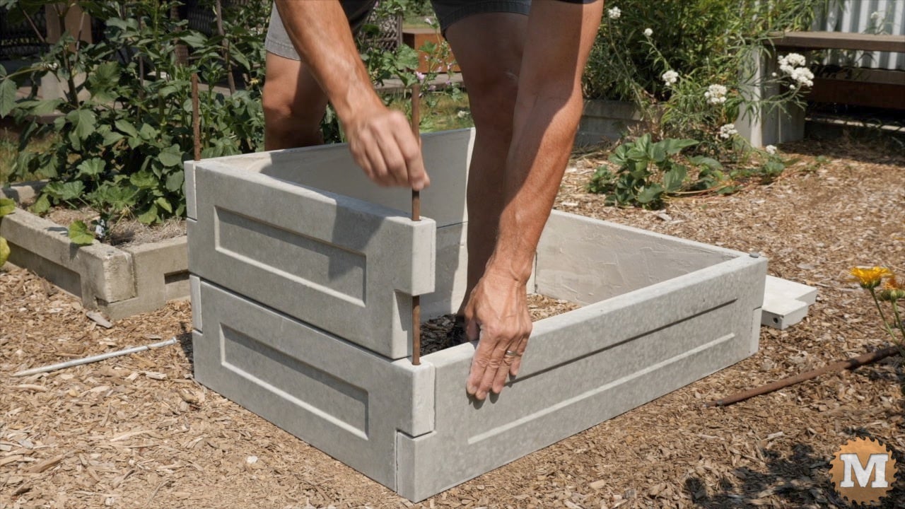 a man assembling cast concrete panels to make a raised bed in the garden