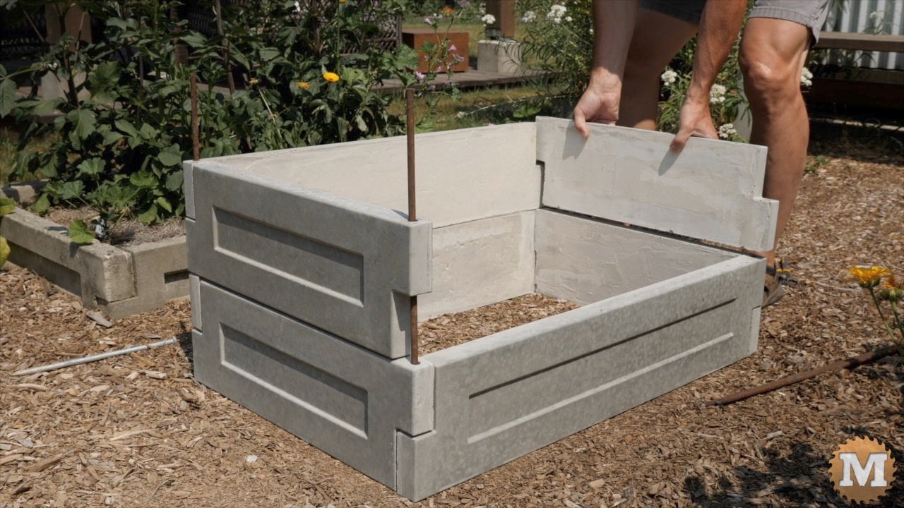 a man assembling cast concrete panels to make a raised bed in the garden