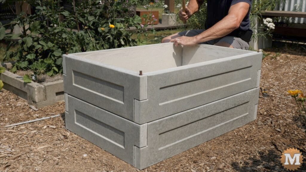 a man assembling cast concrete panels to make a raised bed in the garden
