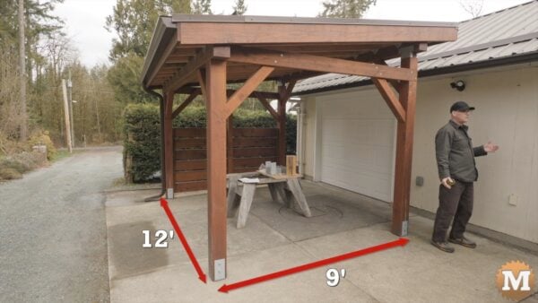 A man talking in front of a wooden lean-to structure