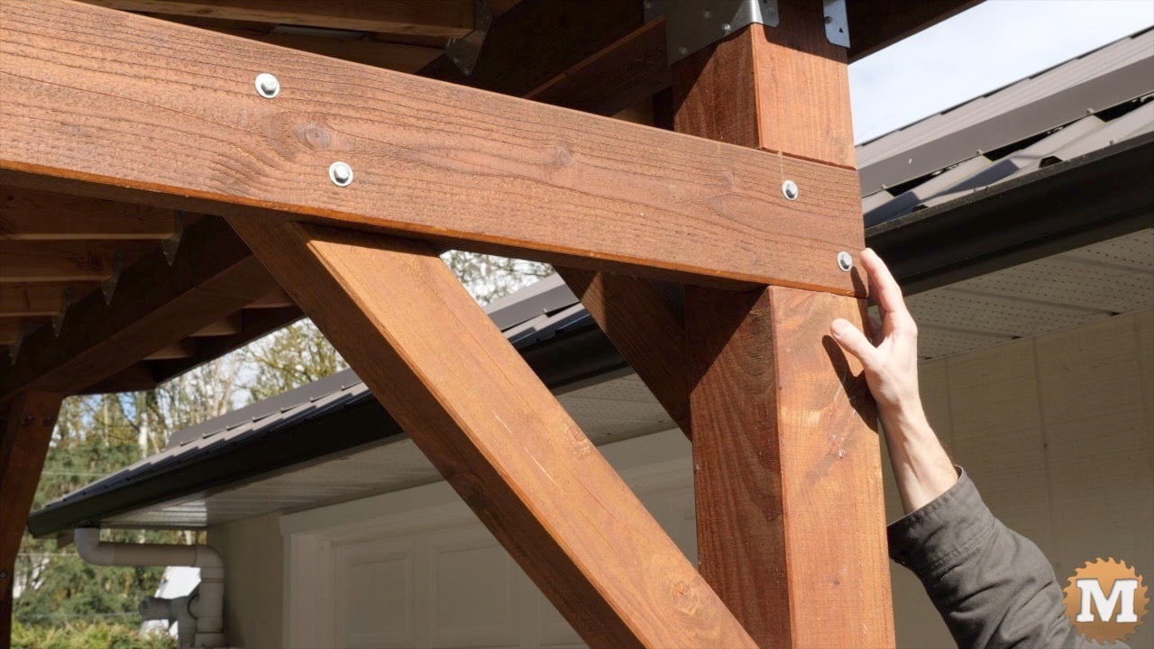 A man pointing to a beam in a post dado of a wooden pavilion