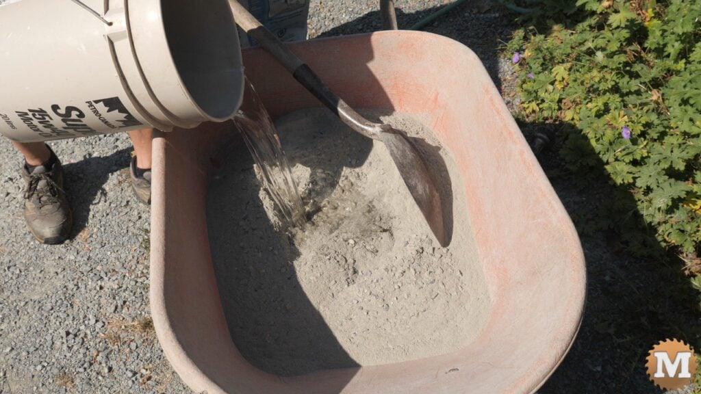 pouring water from a pail onto dry concrete mix in a wheelbarrow