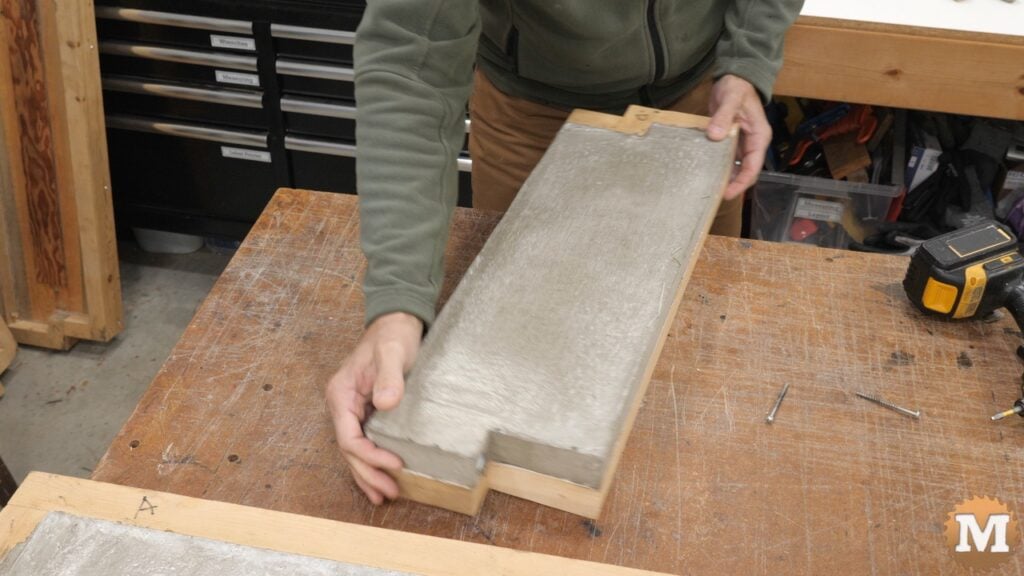A man holding a cast concrete item on a workbench
