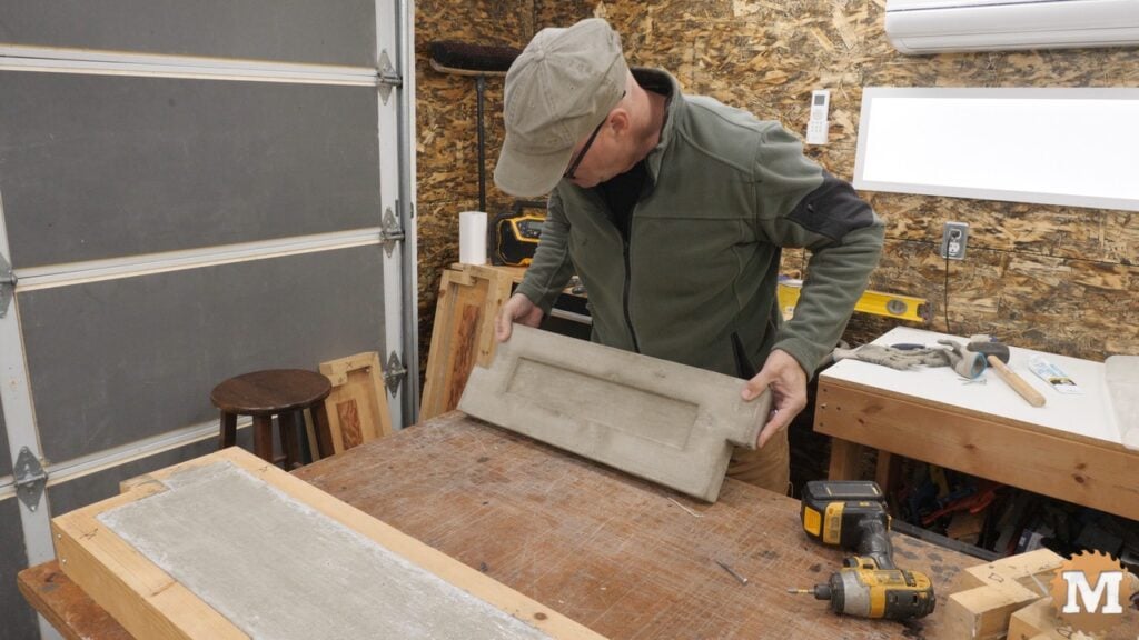 a man holding a cast concrete raised garden bed panel on a workbench