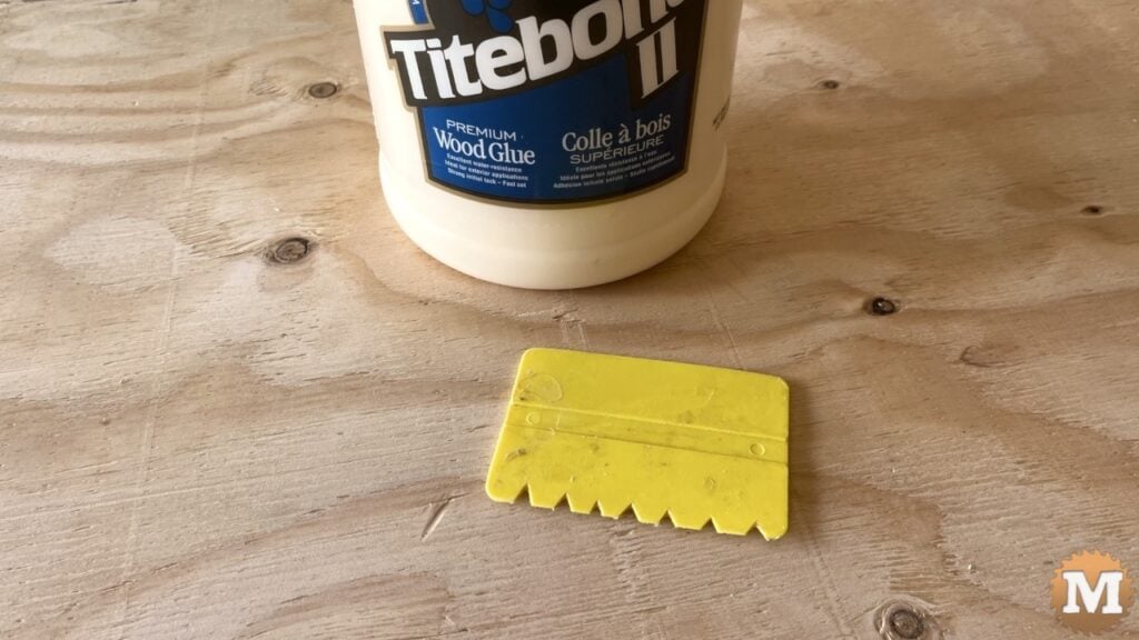a jug of glue and a glue spreader sitting on plywood